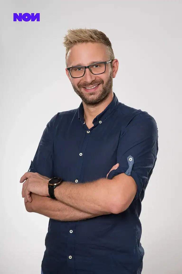 Rafał Moszkowcow Chomsky, International SEO Specialist at non.agency, smiling studio portrait in a navy shirt with arms crossed