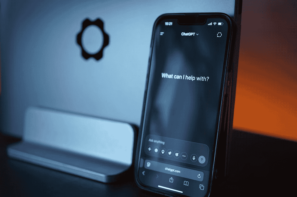 Smartphone displaying the ChatGPT interface in front of a laptop with blue and orange lighting.